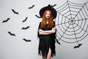 Halloween witch concept - Happy Halloween Witch holding posing over dark grey studio background with bat and spider web.