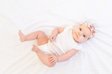 baby girl smiling lying on a white cotton bed at home on her back