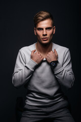 Canvas Print - Informally ( casual ) dressed blonde young man with sharp jawline in his 20's posing in a studio in front of a black background while wearing a white sweater.