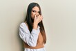Beautiful brunette young woman wearing casual clothes smelling something stinky and disgusting, intolerable smell, holding breath with fingers on nose. bad smell