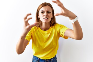 Poster - Young brunette woman standing over isolated background shouting frustrated with rage, hands trying to strangle, yelling mad