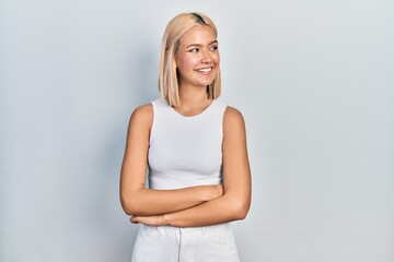 Poster - Beautiful blonde woman wearing casual style with sleeveless shirt looking away to side with smile on face, natural expression. laughing confident.