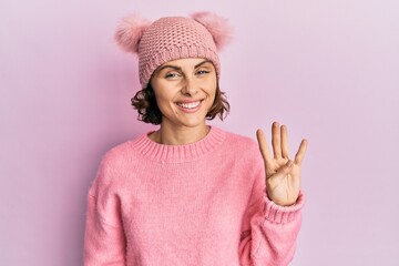 Poster - Young brunette woman wearing cute wool cap showing and pointing up with fingers number four while smiling confident and happy.