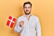 Handsome caucasian man with beard holding denmark flag looking positive and happy standing and smiling with a confident smile showing teeth