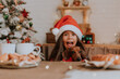 little girl in a Santa hat and a dwarf dachshund want to eat a plate of pastries and a Christmas cake standing on the table in the kitchen decorated for the new year. family tea party. place for text