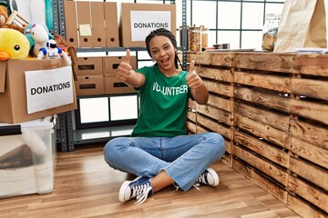 Sticker - Young african american woman wearing volunteer t shirt at donations stand approving doing positive gesture with hand, thumbs up smiling and happy for success. winner gesture.