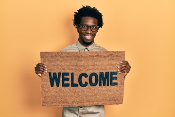 Sticker - Young african american man holding welcome doormat smiling with a happy and cool smile on face. showing teeth.