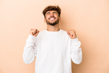 Young arab man isolated on beige background celebrating a victory, passion and enthusiasm, happy expression.