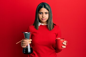 Sticker - Young latin woman holding coffee filter and cup relaxed with serious expression on face. simple and natural looking at the camera.