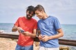 © Krakenimages.com - Two african american man smiling happy using smartphone at the beach.