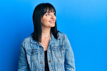 Poster - Young hispanic woman wearing casual denim jacket looking to side, relax profile pose with natural face and confident smile.