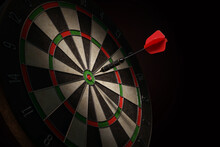 3D Illustration Of A Shiny Black Dart With A Red Flight Hitting The Bulls-eye Of A Dartboard.