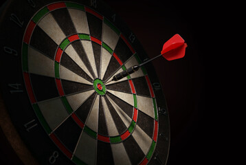 3D illustration of a shiny black dart with a red flight hitting the bulls-eye of a dartboard.