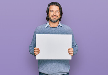 Canvas Print - Middle age handsome man holding blank empty banner looking positive and happy standing and smiling with a confident smile showing teeth