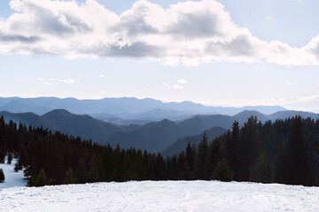 Winter mountain ski resort Pamporovo, Bulgaria. View of snowy ski slope, coniferous forest, dark blue Rhodope Mountains range and dramatic cloudy sky. Beauty of winter nature