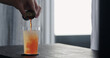 pour orange syrup into lemonade with crushed ice in tumbler glass on oak table