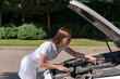 © Vladimir Razgulyaev - car breakdown. the woman lifted the hood of the car, bent over the engine and is trying to independently diagnose the cause of the breakdown and repair the car
