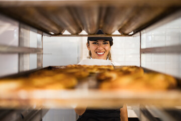 Wall Mural - Beautiful young and happy female worker working in a modern bakery.