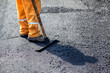 © kalpis - Road construction worker leveling fresh asphalt pavement
