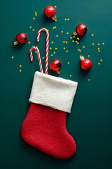 Christmas sock with red balls decorations and candy canes on vintage green background.