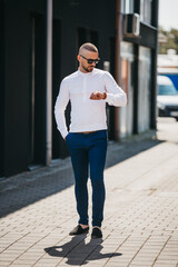 Wall Mural - Cool handsome Caucasian man wearing an elegant white shirt and sunglasses posing outdoor