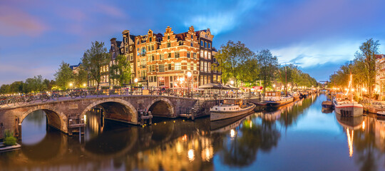 Wall Mural - Amsterdam, Netherlands. Panorama of the historic city center of Amsterdam. Traditional houses and bridges of Amsterdam small town. A romantic evening and a bright reflection of houses in the water. 