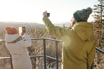 Wall Mural - Young couple with smartphones photographing nature while spending winter day in natural environment