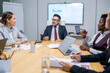 © pressmaster - Large group of intercultural colleagues listening to explanations of confident mature business coach
