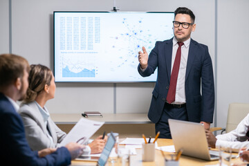 Wall Mural - Serious business coach pointing at one of employees while answering his question during presentation