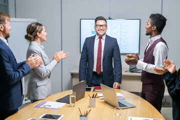 Poster - Intercultural employees standing by large table and clapping hands while congratulating their boss in suit