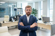 © pressmaster - Happy young businessman with his arms crossed on chest standing against office environment
