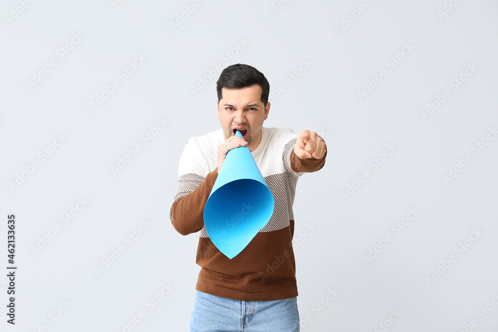 Protesting young man with paper megaphone on light background