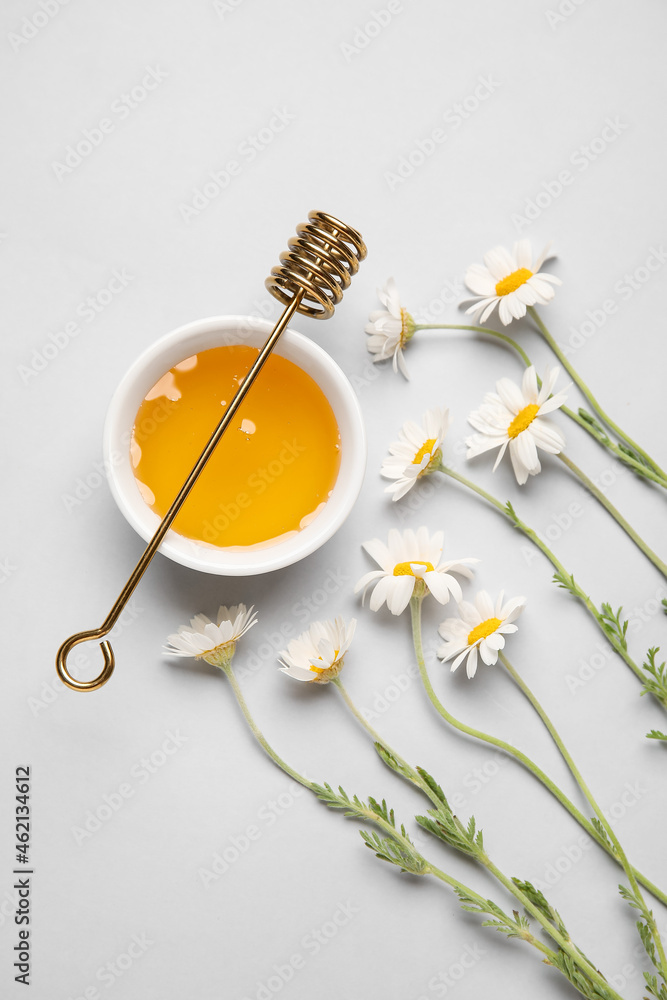 Bowl of honey and chamomile flowers on grey background