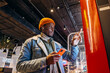 © wifesun - Smiling African-American man in warm denim jacket with wireless earphones uses self-service kiosk to order snack in cafe