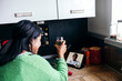 © Westend61 - Mid adult woman having drink during video call in kitchen at home