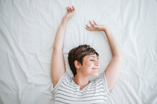 Smiling Woman With Arms Raised Lying On Bed At Home