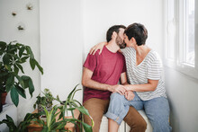 Man And Woman Kissing While Sitting Near Plants At Home