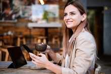 Smiling Businesswoman With Coffee Cup And Smart Phone On Cafe Terrace