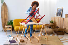 Young woman repairing chair with electric screwdriver in living room