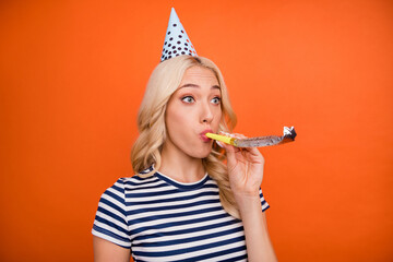 Sticker - Portrait of attractive funny girlish childish girl having fun blowing paper whistle isolated over bright orange color background