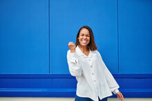 Happy Young Woman Cheering In Front Of Blue Wall