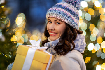 Poster - winter holidays, celebration and people concept - happy smiling woman with christmas gift over festive lights