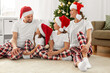 family, winter holidays and christmas concept - happy mother, father and two daughters in santa hats and matching pajamas sittin on floor at home