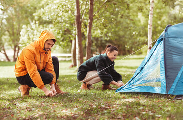 Canvas Print - camping, tourism and travel concept - happy couple setting up tent outdoors