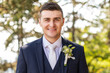 Handsome young groom wearing elegant and stylish dark blue suit outdoors portrait. Happy groom looking and smiling at camera.