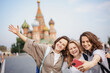 © olezzo - Three beautiful young woman friends making selfie on a smartphone while traveling in Moscow on Red Square