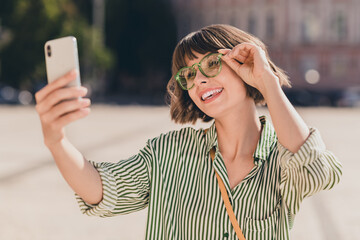 Poster - Photo of positive glad pretty lady hold telephone shoot selfie wear glasses bag striped shirt urban city outside