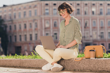 Poster - Photo of cheerful lady sit street hold laptop distance work sunny day wear glasses striped shirt urban city outside