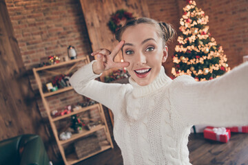 Photo of young cheerful girl happy positive smile show peace cool v-sign make video christmas tree decor lights indoors