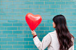 © VISTA by Westend61 - Woman looking at heart shape balloon in front of turquoise brick wall